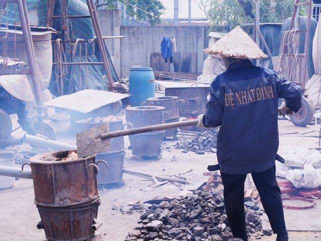 A caster shovelling fuel into the small crucible furnaces in the melting yard