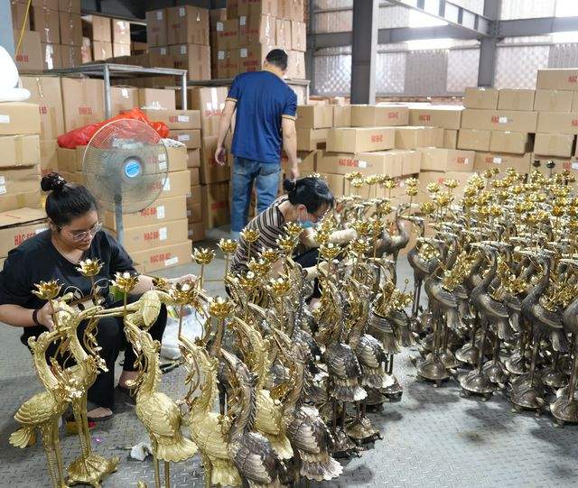 Workers fitting lotus tops to crane-and-tortoise pairs beside cartons marked with the item code