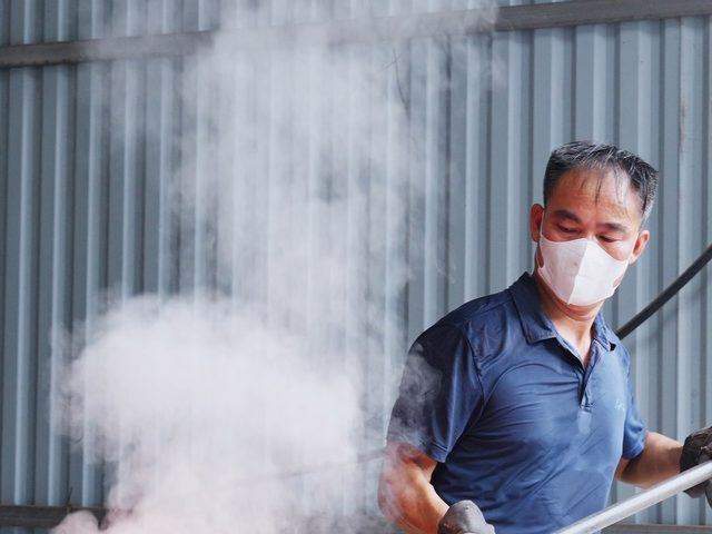 A caster at the furnace mouth, masked and gloved, working the melt