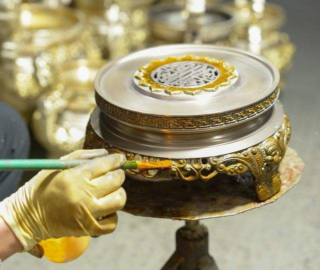 Lacquer being brushed onto a censer lid by hand at the finishing bench
