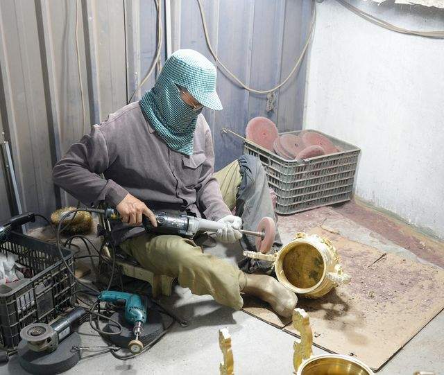A worker polishing the body of a cast bronze censer with a power tool