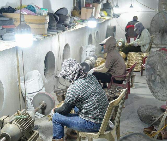 The polishing room: several workers at buffing motors with trays of cast bowls beside them