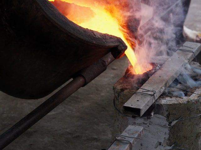 Molten bronze poured from a crucible into a sand mould on the casting floor